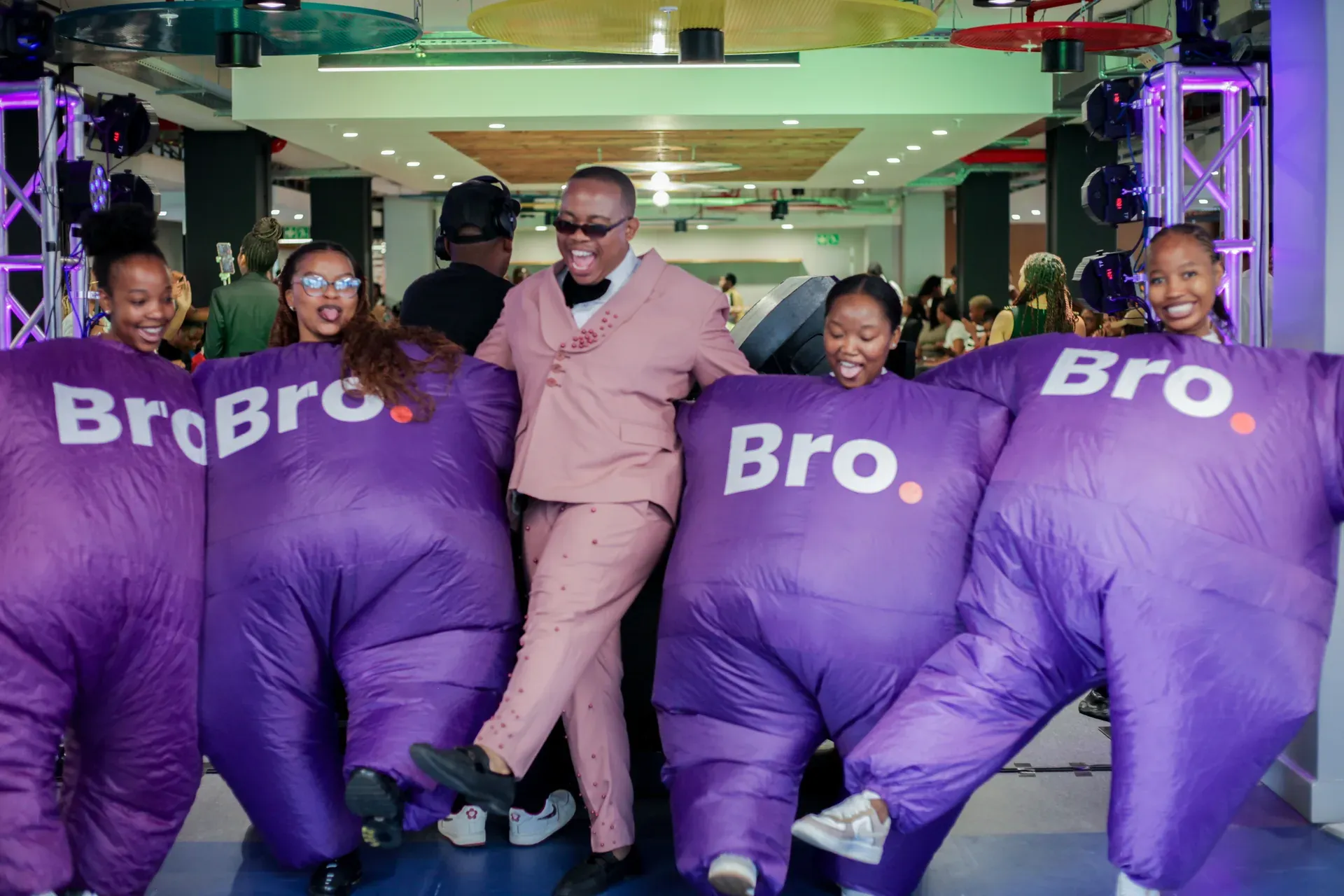 Man in a pink suit dancing with Bro mascots at a Rosebank College activation